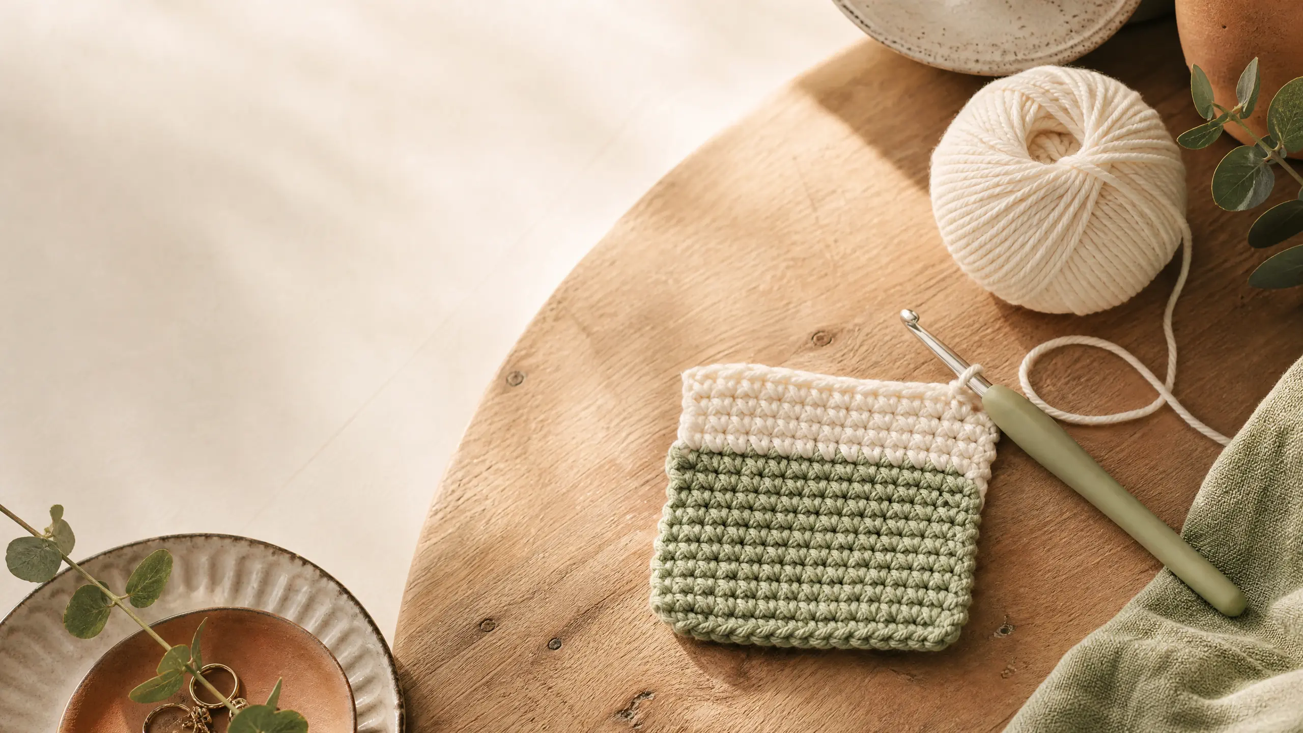 Cream yarn ball, sage-green crochet hook and single crochet swatch on a wooden table